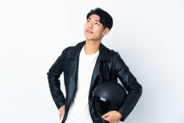 Motosiklet kasklı Çinli bir adam beyaz arka planda izole edilmiş, yukarı bakarken bir fikir düşünüyor.