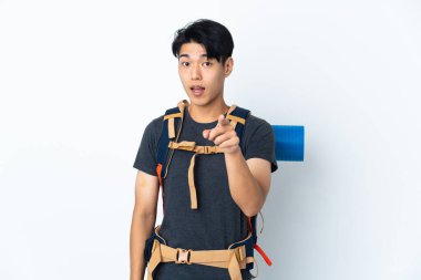 Beyaz arka planda izole edilmiş dağcı Çinli adam şaşırmış ve ön tarafı işaret ediyor.