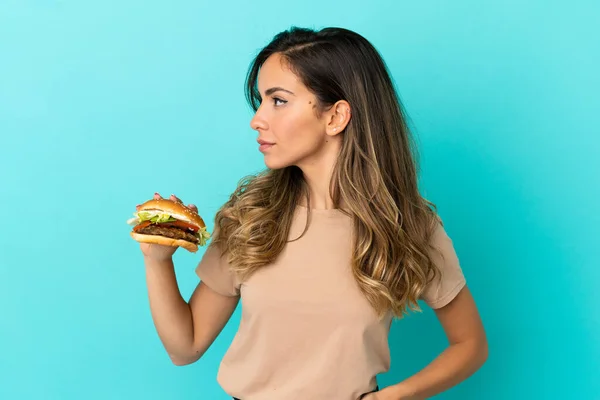 Jeune Femme Tenant Hamburger Sur Fond Isolé Regardant Vers Côté — Photo