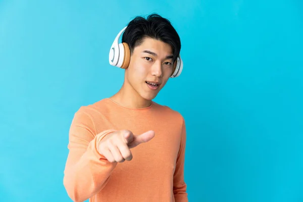 stock image Young Chinese man isolated on blue background listening music