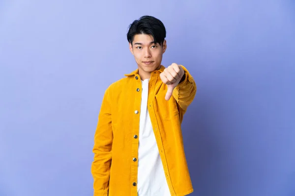 紫色の背景に孤立した若い中国人男性が否定的な表現で親指を示す — ストック写真