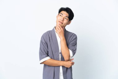 Genç Çinli adam beyaz arka planda izole edilmiş gülümserken yukarı bakıyor.