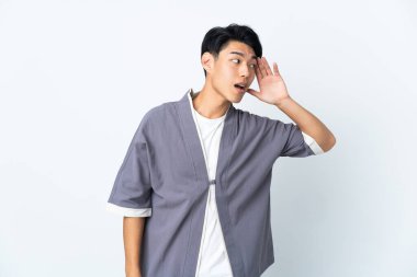 Genç Çinli bir adam beyaz arka planda izole edilmiş. Kulağına elini sürerek bir şeyler dinliyor.