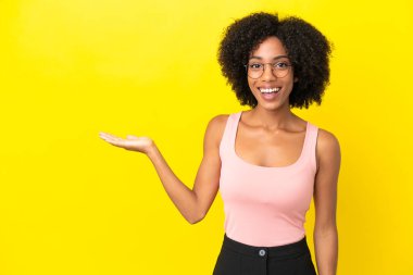 Sarı arka planda izole edilmiş genç Afrikalı Amerikalı bir kadın. Avucunun içinde hayali bir ilan tutuyor.