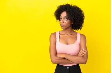 Sarı arka planda izole edilmiş genç Afrikalı Amerikalı kadın kollarını kavuşturuyor.