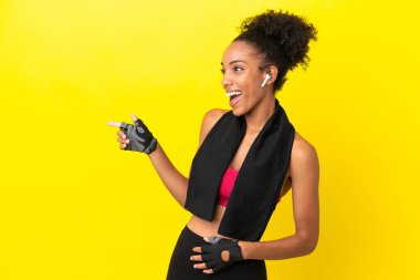 Sarı arka planda izole edilmiş genç Afrikalı sporcu kadın parmağını yana uzattı ve bir ürün sundu.