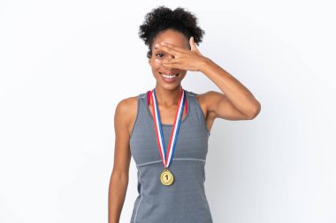 Beyaz arka planda madalyaları olan genç Afrikalı Amerikalı kadın gözleri elleriyle kaplıyor ve gülümsüyor.