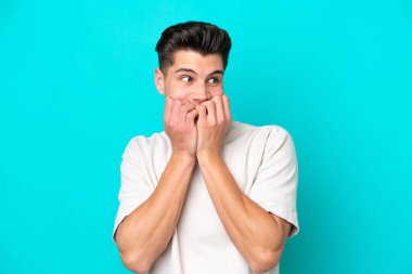 Genç, yakışıklı, beyaz bir adam mavi bakkalda izole edilmiş. Gergin ve korkmuş. Elleri ağıza alıyor.