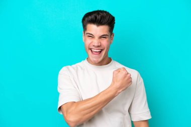 Genç, yakışıklı, beyaz bir adam mavi bir bakkalda izole edilmiş bir şekilde zaferi kutluyor.