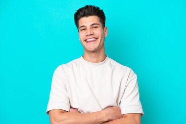 Genç, yakışıklı, beyaz bir adam, mavi bir bakkalda izole edilmiş, kollarını ön cephede çapraz tutuyor.