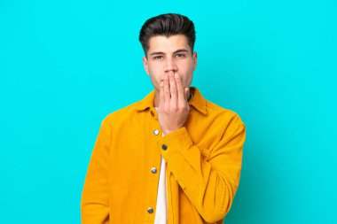 Genç, yakışıklı, beyaz bir adam mavi bir bakkalda izole edilmiş. Ağzını eliyle kapatıyor.