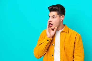 Genç, yakışıklı, beyaz bir adam, mavi bir bakkalda izole edilmiş. Yan tarafa bakarken sürpriz bir jest yapıyor.