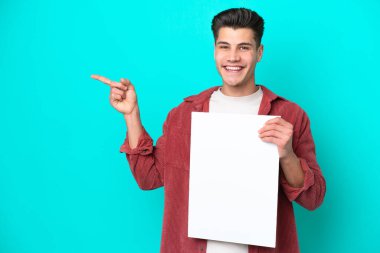 Genç, yakışıklı, beyaz bir adam mavi bir bakkalda izole edilmiş. Elinde boş bir levha var ve onu işaret ediyor.