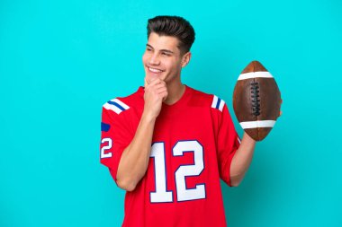 Genç beyaz adam ragbi oynuyor. Mavi arka planda izole edilmiş. Yan tarafa bakıyor ve gülümsüyor.