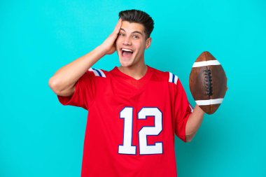Genç beyaz adam rugby oynuyor. Mavi arka planda izole edilmiş, sürpriz bir ifadeyle.