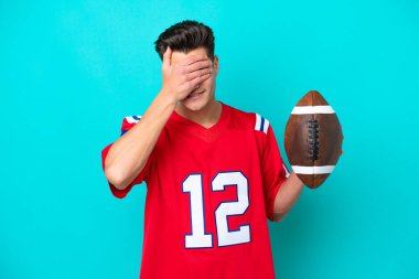 Rugby oynayan Kafkasyalı genç adam mavi arka planda izole edilmiş, yorgun ve hasta bir ifadeyle.