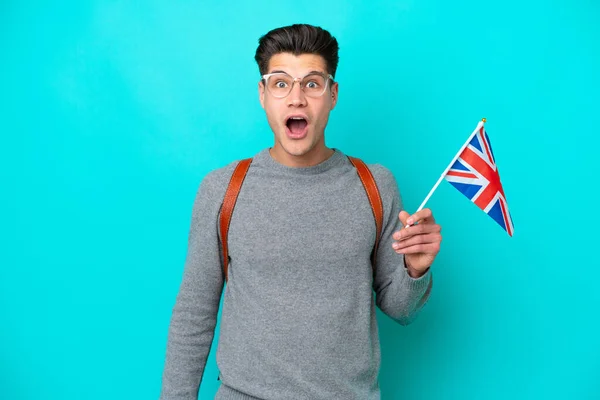 青い背景にイギリス国旗を掲揚している若い白人男性は驚きの表情で — ストック写真