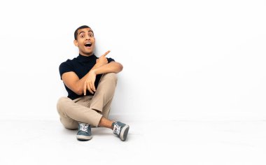 Afro-Amerikan adam yerde oturuyor, şaşırmış ve işaret ediyor.