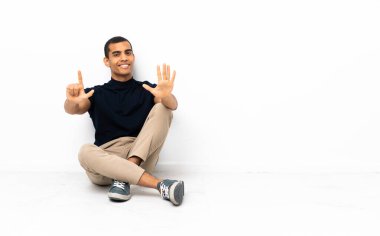 Afro-Amerikalı adam yerde oturmuş parmaklarıyla yediyi sayıyor.