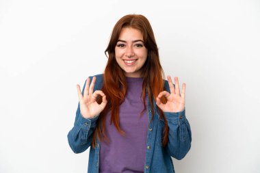 Beyaz arka planda izole edilmiş genç kızıl saçlı kadın iki eliyle onay işareti gösteriyor.