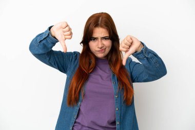 Beyaz arka planda izole edilmiş genç kızıl saçlı kadın baş parmağını iki eliyle aşağı gösteriyor.