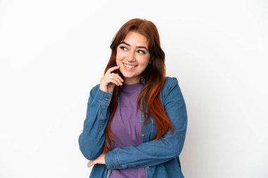 Genç kızıl saçlı kadın, beyaz arka planda izole edilmiş bir şekilde bakarken bir fikir düşünüyor.