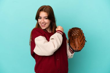 Beyzbol oynayan genç kızıl saçlı kadın mavi arka planda izole bir şekilde zaferi kutluyor.