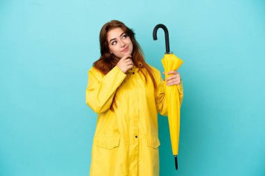 Mavi arka planda şemsiyesi olan kızıl saçlı kadın yukarı bakıyor.