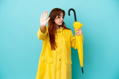 Mavi arka planda şemsiyesi olan kızıl saçlı kadın dur hareketi yapıyor ve hayal kırıklığına uğruyor.