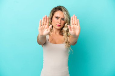 Mavi arka planda izole edilmiş genç Brezilyalı kadın dur hareketi yapıyor ve hayal kırıklığına uğruyor.