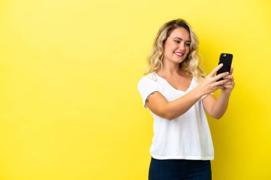 Sarı arka planda izole edilmiş genç Brezilyalı bir kadın selfie çekiyor.