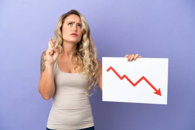 Mor arka planda izole edilmiş genç Brezilyalı bir kadın azalan bir istatistik okuyla işaret tutuyor ve parmaklarını çapraz yapıyor.