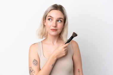 Beyaz arka planda izole edilmiş beyaz bir kadın elinde makyaj fırçası ve yukarı bakıyor.