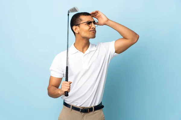 在孤立的蓝色背景上打高尔夫的非裔美国人 他的面部表情令人困惑 — 图库照片