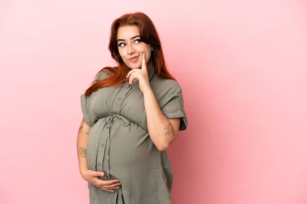 Νεαρή Κοκκινομάλλα Καυκάσια Γυναίκα Απομονωμένη Ροζ Φόντο Έγκυος Και Σκέφτεται — Φωτογραφία Αρχείου