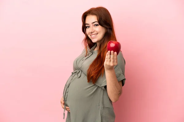 年轻红头发的高加索女人 身孕粉红背景 拿着一个苹果 — 图库照片