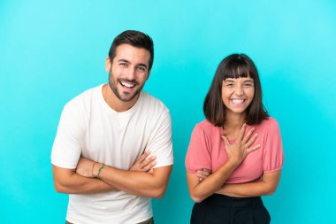 Mavi arka planda izole edilmiş genç bir çift gülümserken kollarını çapraz tutuyor.