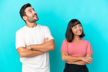 Mavi arka planda izole edilmiş genç çift gülümserken yukarı bakıyor