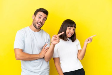 Young couple isolated on yellow background pointing finger to the side in lateral position