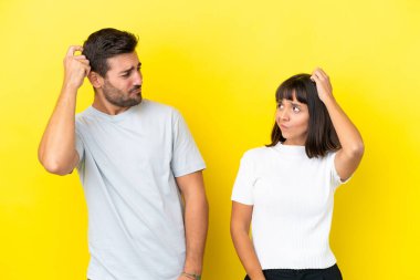 Young couple isolated on yellow background having doubts while scratching head