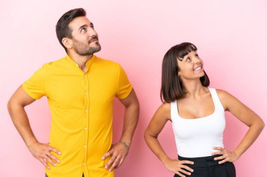 Genç çift pembe arka planda izole edilmiş kolları kalçalarında poz veriyor ve gülüyorlar.