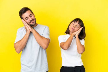 Sarı arka planda izole edilmiş genç bir çift uyku jesti yapıyor.