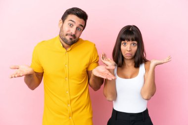 Pembe arka planda izole edilmiş genç bir çift omuzlarını kaldırırken önemsiz bir jest yapıyor.