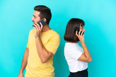 Mavi arka planda izole edilmiş genç bir çift cep telefonuyla sohbet ediyorlar.