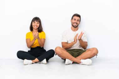 Yerde oturan genç çift, beyaz arka planda izole bir şekilde bir konferansta sunumdan sonra alkışlıyorlar.