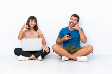 Yerde oturan genç çift, beyaz arka planda izole edilmiş cep telefonu ve cep telefonlarını tutarak telefon ediyorlar. Bana geri dönüş işareti ver.