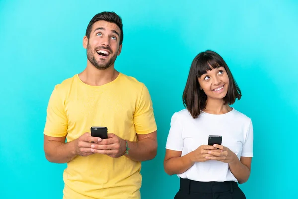 Stock image Young couple isolated on blue background using mobile phone and looking up