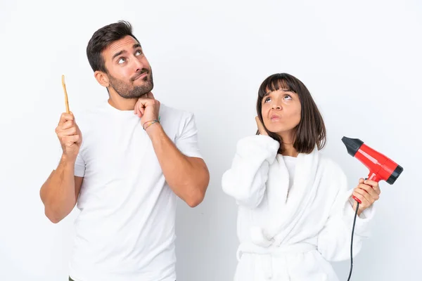 Young Caucasian Couple Holding Hairdryer Toothbrush Isolated White Background Thinking — Stok fotoğraf