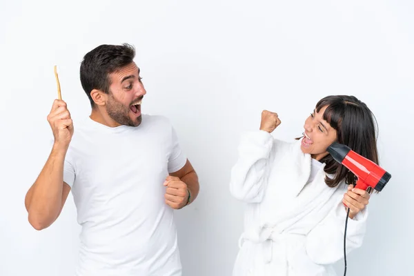 Young Caucasian Couple Holding Hairdryer Toothbrush Isolated White Background Celebrating — Φωτογραφία Αρχείου