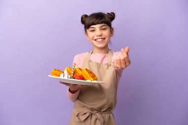 Mor arka planda izole edilmiş waffle tutan küçük beyaz kız para hareketi yapıyor.